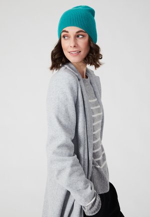 Cardigan grigio e maglione a righe con un berretto a coste color teal. Textura morbida, vestibilità rilassata e look a strati con maniche lunghe.
