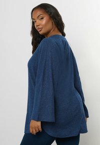 Navyblaues, strukturiertes Oberteil mit lockerer Passform, weiten Ärmeln und abgerundetem Saum. Das weiche Material und das dezente Muster verleihen einen lässigen Look.