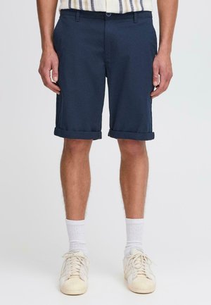 Pantaloni corti in cotone blu navy con vestibilità slim, risvolti e passanti per cintura. Abbinati a calze sportive bianche e sneaker beige.