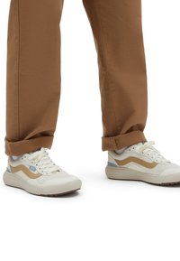 Weiße Sneakers mit braunen und blauen Akzenten, strukturiertem Obermaterial, abgerundeter Zehenpartie und Schnürverschluss; kombiniert mit hochgekrempelten braunen Hosen.