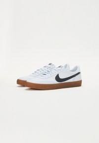 Vita lädersneakers med en svart swoosh-logotyp, gummisula och ljusblå accenter på snörning och tunga.