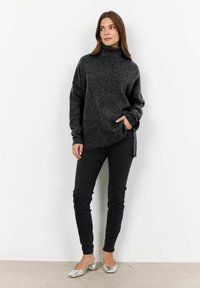 Overmaatse antracietgrijze coltrui met ribgebreide manchetten, zijopeningen en een zachte textuur, gecombineerd met zwarte slim-fit broek en zilveren ballerina's.