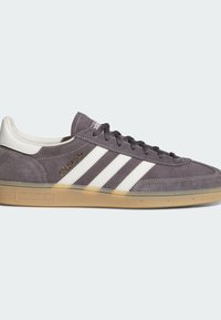 Szare zamszowe sneakersy Adidas z białymi paskami, gumową podeszwą, czarnymi sznurówkami i złotym napisem "Spezial" z boku.