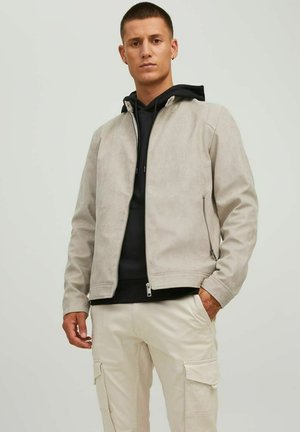 Light gray suede jacket with a front zipper, side pockets, and a minimalist design, worn over a black hoodie and cream cargo pants.