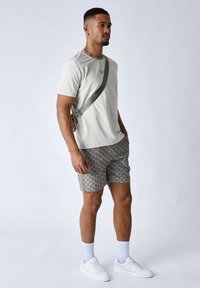 Camiseta gris claro, pantalones cortos con estampado en gris y blanco, zapatillas blancas y calcetines de caña baja. Correa cruzada y pequeño logo en la camiseta.