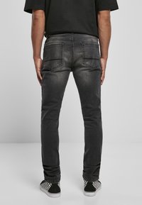 Jeans de mezclilla negra con corte ajustado, que cuentan con bolsillos traseros, sutiles desgastes y una superficie ligeramente texturizada. Combinados con zapatos sin cordones de cuadros.