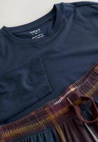 Navyblaues Rundhalsausschnitt-T-Shirt mit einer Tasche, kombiniert mit karierten Lounge-Shorts in Burgunderrot, Gelb und Weiß. Aus weichem Baumwollstoff.