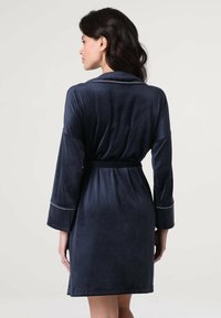 Robe in velluto blu navale con design avvolgente, maniche lunghe e vita legata. Presenta piping bianco lungo i polsini e il colletto per un contrasto.