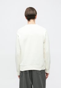 Λευκό πλεκτό πουλόβερ με στρογγυλή λαιμόκοψη και μανσέτες με ριμπ σχέδιο, με ομαλή υφή και άνετη γραμμή, συνδυασμένο με γκρι ριγέ παντελόνι.