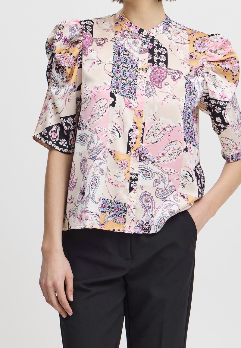 Blouse à manches courtes en tissu semblable à la soie, présentant un mélange de motifs pastel, des manches bouffantes, une fermeture à boutons sur le devant et un col mandarin.
