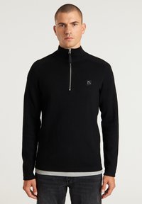Schwarzer Reißverschluss-Pullover aus Strickstoff mit hohem Kragen, langen Ärmeln und einem kleinen Logopatch auf der linken Brust.