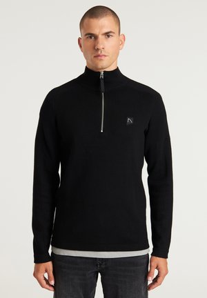 Schwarzer Reißverschluss-Pullover aus Strickstoff mit hohem Kragen, langen Ärmeln und einem kleinen Logopatch auf der linken Brust.