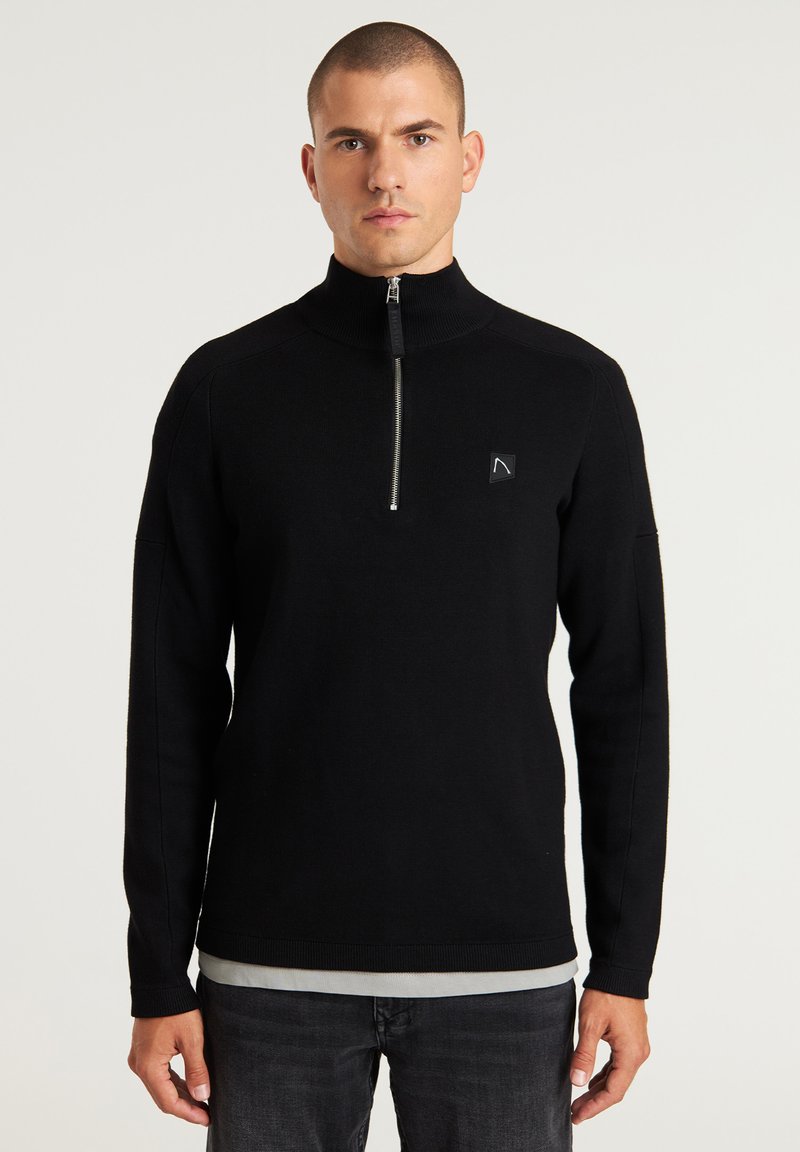 Schwarzer Reißverschluss-Pullover aus Strickstoff mit hohem Kragen, langen Ärmeln und einem kleinen Logopatch auf der linken Brust.