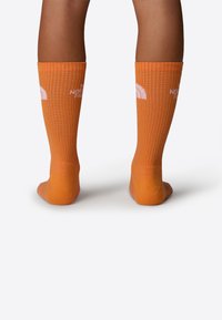 Medias naranjas hasta la rodilla con textura acanalada y detalle del logotipo en blanco de The North Face. El material parece duradero y elástico.