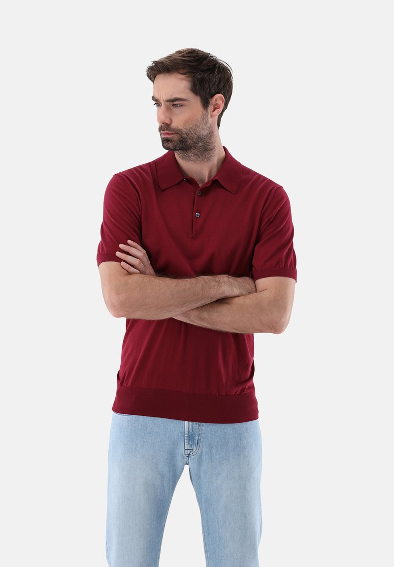 Rotes Poloshirt mit kurzen Ärmeln und Kragen, ausgestattet mit einer Knopfleiste und ribbedem Saum, kombiniert mit hellblauen Jeans. Glatte Textur.