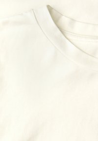 Roomkleurig katoenen t-shirt met een ronde hals en een zachte textuur, met een gladde stof en een ingetogen ontwerp zonder patronen of accenten.