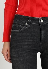 Svarta jeans i denim med hög midja, utrustade med fem fickor och silverdetaljer. Tyget har en något texturerad yta.