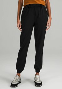 Czarne spodnie dresowe z elastycznym pasem i ściągaczami na kostkach, wykonane z miękkiego materiału. W połączeniu z szarymi trampkami z czarnymi akcentami.