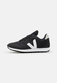 Black athletic shoe with a white V logo, textured fabric upper, padded collar, and rubber sole. Features a low profile and lace-up design.