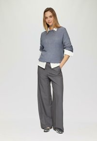 Pull en maille bleu clair avec un motif texturé, superposé à une chemise blanche à col ; associé à un pantalon large gris et des chaussures noires brillantes.