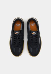 Mustat Nike SB -kengät, joissa on sileä nahkainen ja mokkainen päällinen, oranssi sisäpohja, mustat nauhat ja vaaleanruskea kumipohja. Kengän kielellä on logo.