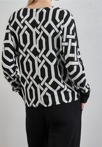 Svart och grå stickad tröja med geometriskt mönster, långa ärmar, rund halsringning och ribbade muddar. Avslappnad passform, texturerad tyg.