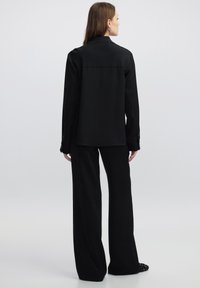 Camicia nera con bottoni, a maniche lunghe, con una vestibilità rilassata e un retro di lunghezza media. Abbinata a pantaloni neri a gamba larga.