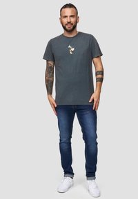 Grijze katoenen t-shirt met ronde hals en een klein grafisch ontwerp op de borst, gepaard met blauwe denim jeans en witte sneakers.