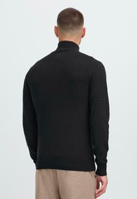 Pull noir avec un col montant, des manches longues, des poignets et un ourlet côtelés, fabriqué dans un matériau lisse et doux, design ajusté.