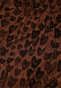 Brauner Stoff mit einem schwarzen Leopardenmuster, das eine glatte Textur und geschichtete Falten aufweist. Das Design enthält unterschiedliche Mustergrößen und -formen.
