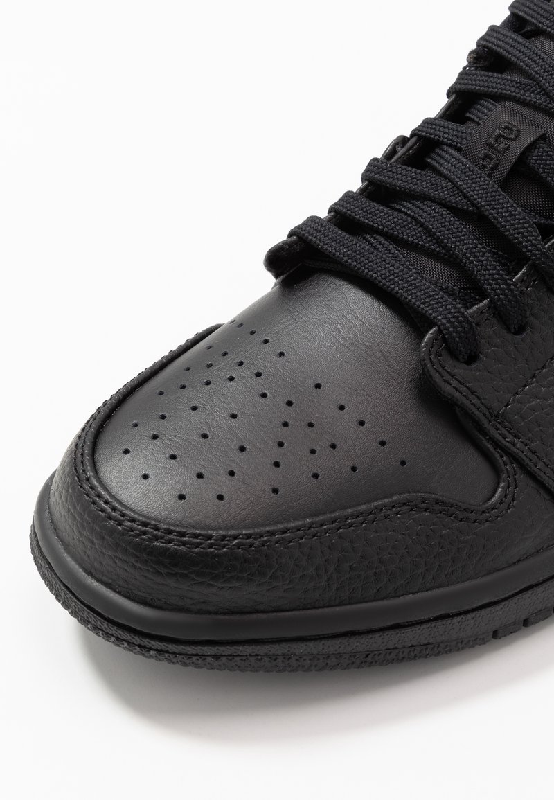 Schwarze Sneaker aus strukturiertem Leder mit perforiertem Design an der Zehenpartie, flachen schwarzen Schnürsenkeln und einer Gummisohle.