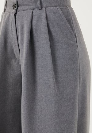 Pantalon gris taille haute avec plis sur le devant, poches latérales, passants pour ceinture et fermeture par bouton, présenté de la taille jusqu'au milieu des cuisses.
