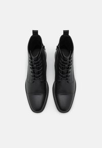Bottines noires en cuir avec bout arrondi, empeigne texturée, lacets à l'avant et boucle à l'arrière pour un enfilage facile.