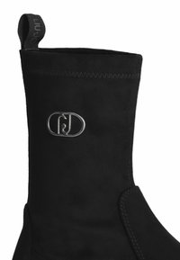 Stivaletto alla caviglia in suede nera con finitura testurizzata, caratterizzato da una cucitura e un accento con logo argentato sul lato.