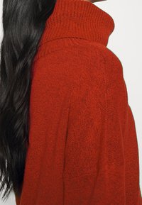 Maglione rosso lavorato a maglia con collo alto e tessuto strutturato, caratterizzato da una vestibilità comoda e un motivo sottile su tutta la superficie.