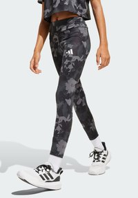 Leggings de patrón floral en negro y gris, hechos de un tejido elástico, combinados con zapatillas deportivas blancas y negras y calcetines tipo crew blancos.