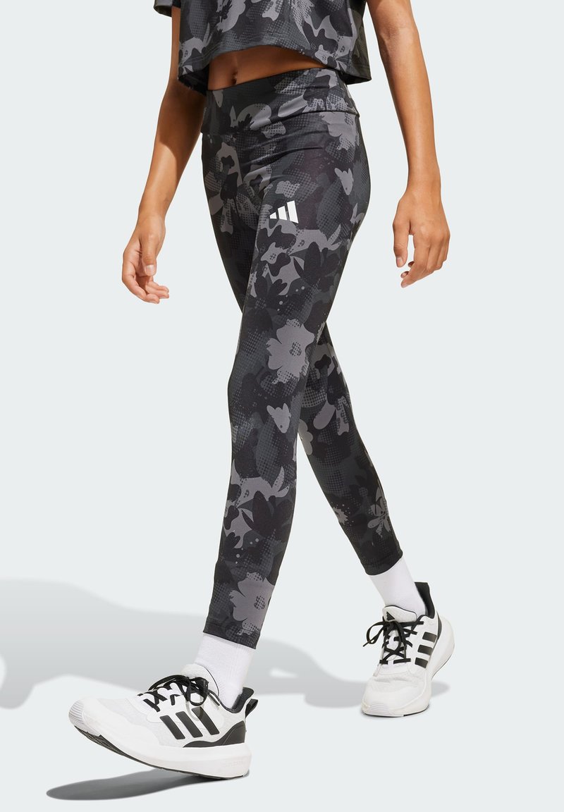 Leggings de patrón floral en negro y gris, hechos de un tejido elástico, combinados con zapatillas deportivas blancas y negras y calcetines tipo crew blancos.