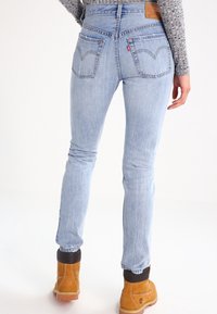 Vaqueros ajustados de denim azul claro con una cintura alta, que cuentan con dos bolsillos traseros y sutiles detalles de costura. Combinados con botas de trabajo marrones.