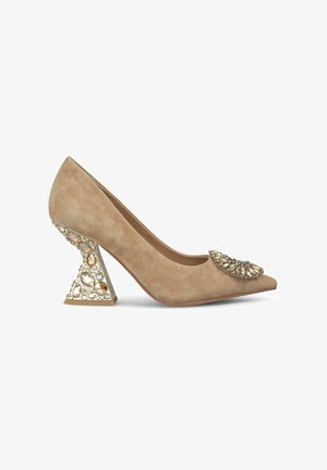 Escarpins en suède beige à talon haut avec un bout pointu et un talon triangulaire orné de bijoux décorés de pierres transparentes et ambrées.