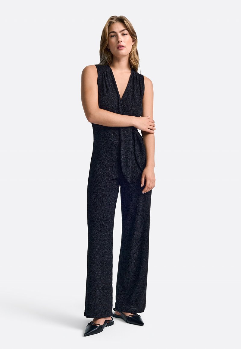 Mustmust pihtkätega jumpsuit, millel on sügava V-kaeluse disain, millel on sile tekstuur ja voolav stiil. Sobib teravate mustade kingadega.