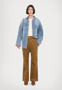 Suuruse järgi oversize denim särg, valge ribidega sviiter, pruunid sametpüksid ja pruunid kingad. Tähelepanu pöörates vabale lõikele ja kontrastsetele värvidele.