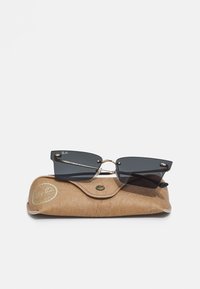 Occhiali da sole neri rettangolari con un ponte in metallo dorato, appoggiati su una custodia strutturata color beige con un logo circolare e chiusura a scatto.