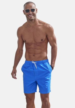 Blaue Badehose mit elastischem Bund und weißem Kordelzug. Glattes Material, reguläre Passform und Seitentaschen. Trägt eine Sonnenbrille.