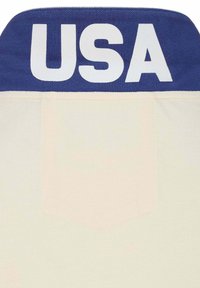 Maglia atletica bianca con colletto blu, caratterizzata da grandi lettere bianche "USA" nella parte superiore. Tessuto texturizzato con dettagli di cucitura visibili.