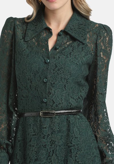 Grünes Spitzendress mit Knopfverschluss vorne, spitzem Kragen und langen puffärmel. Hat einen schwarzen Gürtel in Taille für zusätzliche Definition.