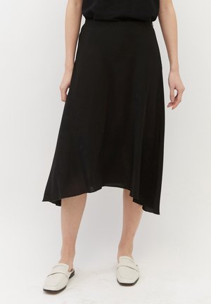 Schwarzer Midirock aus glattem Stoff, mit asymmetrischem Saum und einem verdeckten Seitenreißverschluss. Kombiniert mit hellen Slip-on-Schuhen.