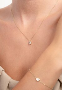 Gouden ketting met een heldere ovale edelsteen, fijne ketting. Een bijpassende gouden armband heeft ook een heldere ovale edelsteen, beide tegen blote huid.