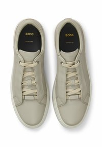 Beige leather sneakers with a smooth texture, round toe, flat laces, and rubber sole. Features branding on the insole in gold. Crafted in Italy.