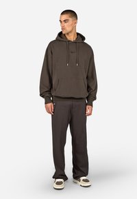 Dunkelbraun Kapuzenpullover mit Kordeln und Vordertasche, kombiniert mit passenden dunklen Hosen und hellen Sneakern. Glatte Textur.