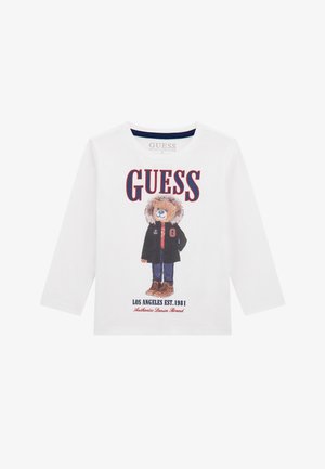Biała koszulka z długim rękawem wykonana z organicznej bawełny, z graphicznym motywem niedźwiedzia w kurtce i brązowych butach. Tekst zawiera "GUESS" oraz "LOS ANGELES EST. 1981."